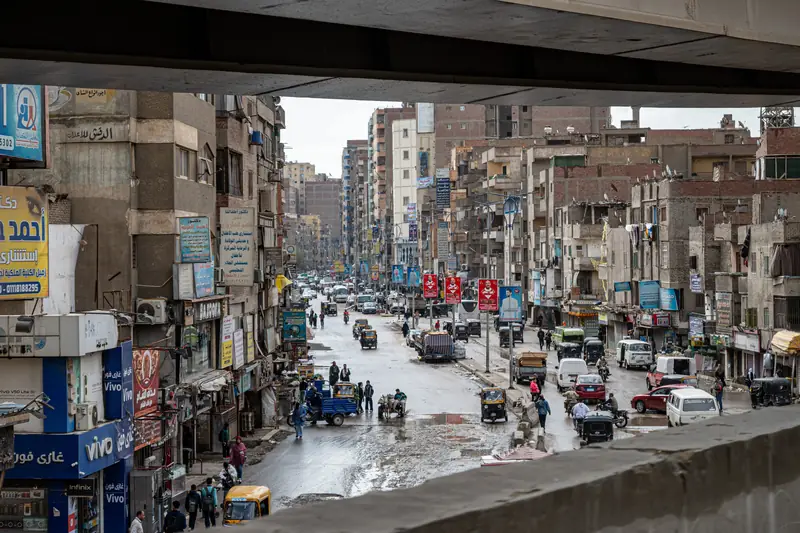 Belebte Straße in Kairo mit Autos, Tuk-Tuks und hohen Wohnhäusern, von einer Brücke aus