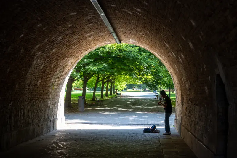 Ein Musiker spielt im Schatten eines Tunnels, dahinter ein sonniger Park